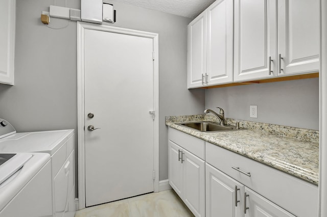 clothes washing area with cabinets, a textured ceiling, washer and clothes dryer, and sink