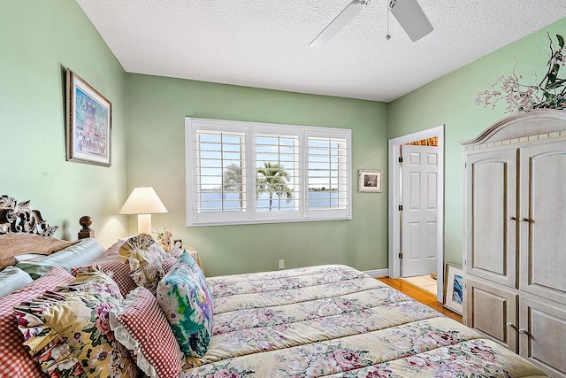 bedroom with ceiling fan, light wood-type flooring, and a textured ceiling