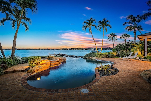 pool at dusk featuring a patio and a water view