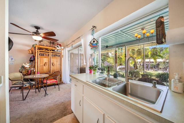 kitchen featuring light colored carpet, a healthy amount of sunlight, sink, and white cabinets