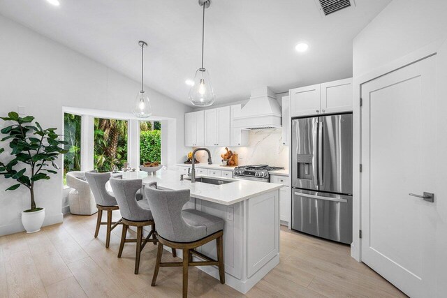 kitchen with a kitchen island with sink, sink, white cabinets, lofted ceiling, and stainless steel appliances