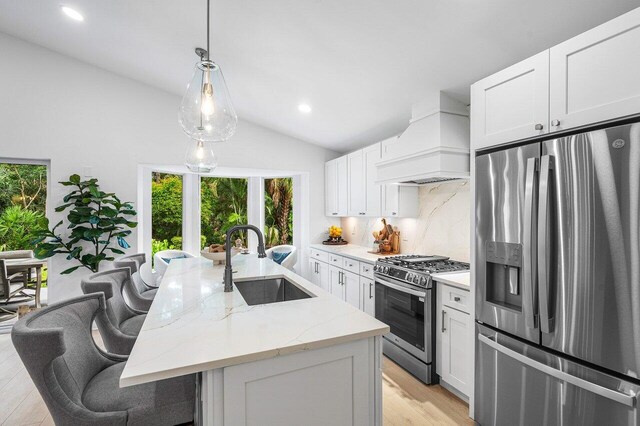 kitchen with appliances with stainless steel finishes, premium range hood, light stone counters, a center island with sink, and sink