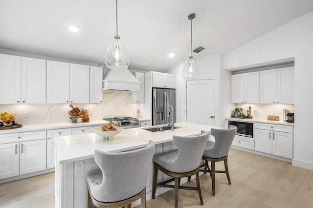 kitchen with white cabinets, premium range hood, appliances with stainless steel finishes, and vaulted ceiling