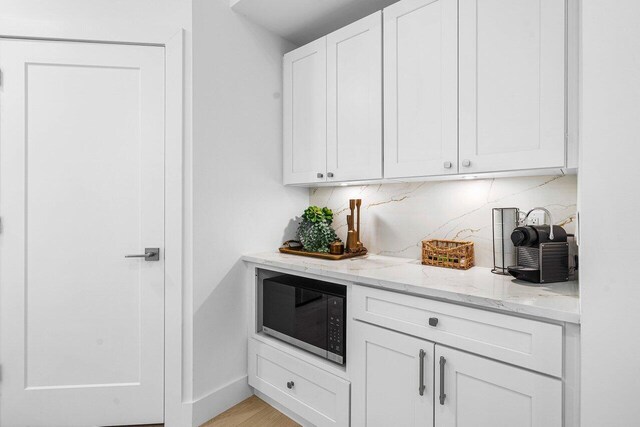 bar featuring light wood-type flooring, tasteful backsplash, light stone counters, and white cabinets