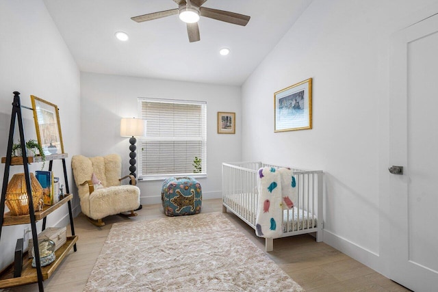 bedroom featuring light hardwood / wood-style floors, lofted ceiling, ceiling fan, and a nursery area