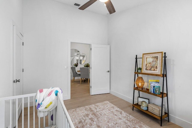 bedroom featuring ceiling fan, a nursery area, and light hardwood / wood-style flooring