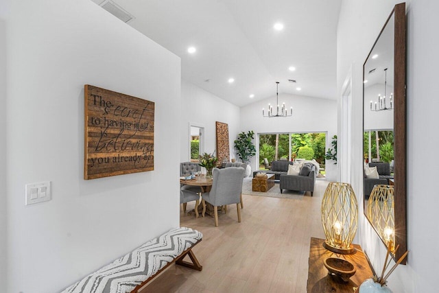 corridor featuring light wood-type flooring, an inviting chandelier, and high vaulted ceiling