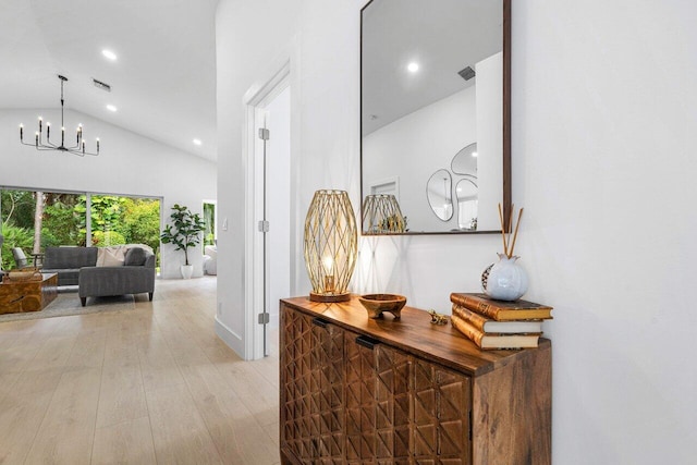 corridor with an inviting chandelier, light hardwood / wood-style floors, and high vaulted ceiling