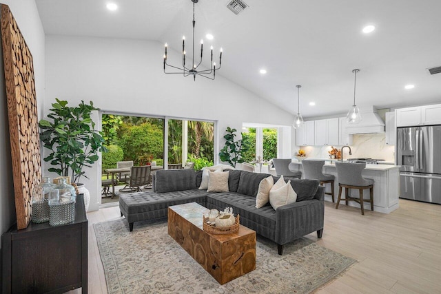 living room featuring an inviting chandelier, light hardwood / wood-style floors, and high vaulted ceiling