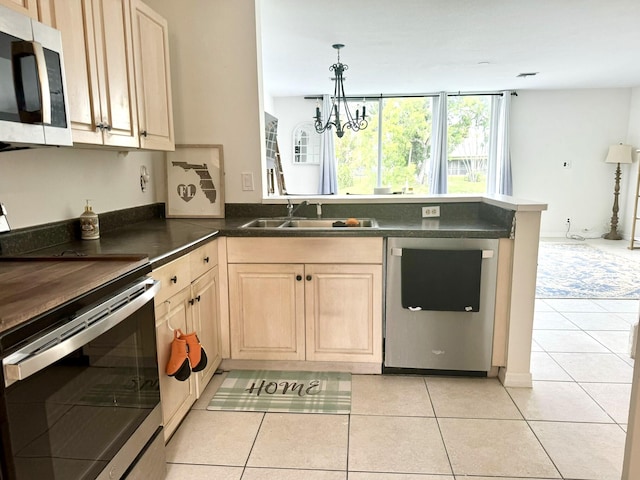 kitchen with appliances with stainless steel finishes, light tile patterned flooring, kitchen peninsula, sink, and a chandelier