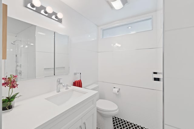 bathroom with tile patterned floors, toilet, a tile shower, and vanity