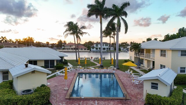 pool at dusk with a patio area, a lawn, central AC, and a water view