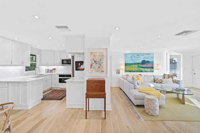 kitchen featuring light hardwood / wood-style floors, sink, stainless steel oven, black microwave, and white cabinets