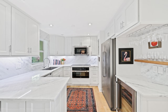 kitchen featuring light hardwood / wood-style flooring, backsplash, appliances with stainless steel finishes, kitchen peninsula, and sink