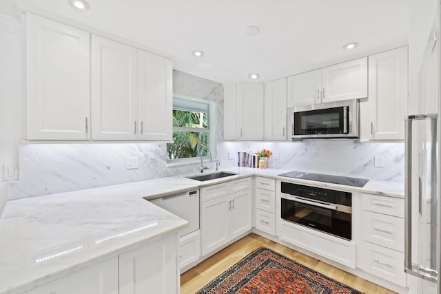 kitchen with appliances with stainless steel finishes, light hardwood / wood-style flooring, sink, and light stone countertops