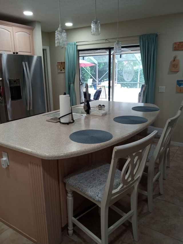 kitchen featuring an island with sink, light countertops, a kitchen breakfast bar, stainless steel refrigerator with ice dispenser, and hanging light fixtures