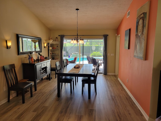 dining space with lofted ceiling, wood-type flooring, and a textured ceiling