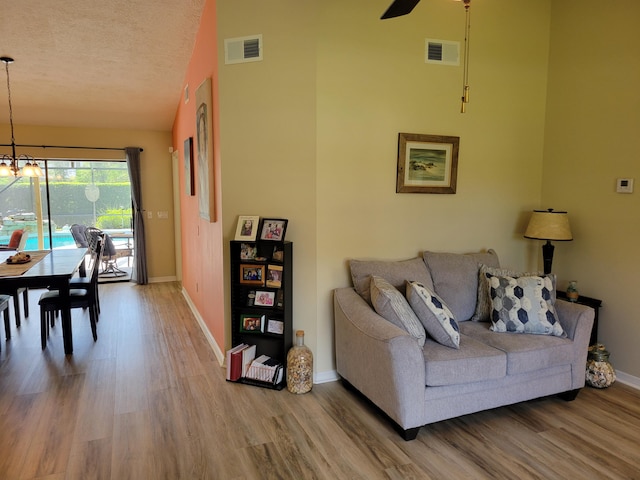 living room featuring vaulted ceiling, ceiling fan with notable chandelier, wood-type flooring, and a textured ceiling