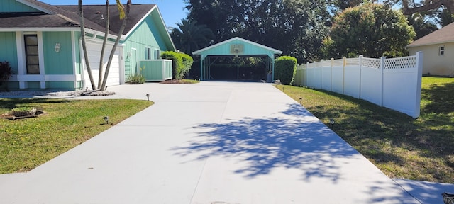 view of yard featuring a detached carport, concrete driveway, fence, and a garage