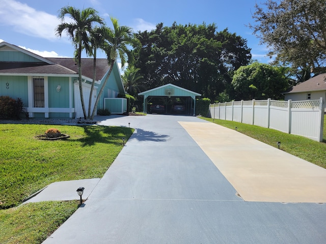 exterior space with a detached carport, concrete driveway, a front yard, and fence