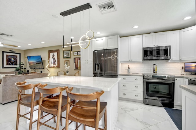 kitchen with white cabinets, decorative light fixtures, stainless steel appliances, a kitchen bar, and tasteful backsplash