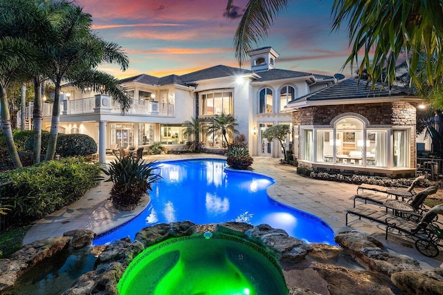 pool at dusk featuring an in ground hot tub and a patio