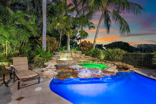 pool at dusk with a patio area and an in ground hot tub