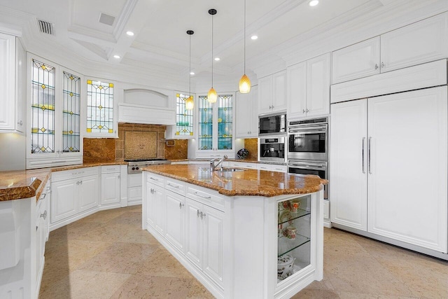 kitchen featuring built in appliances, pendant lighting, tasteful backsplash, a kitchen island with sink, and white cabinets