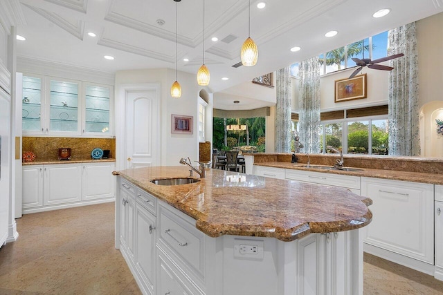 kitchen featuring pendant lighting, an island with sink, sink, white cabinetry, and ceiling fan