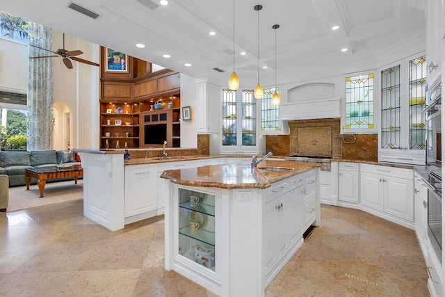 kitchen with ceiling fan, light stone countertops, a kitchen island with sink, and white cabinetry