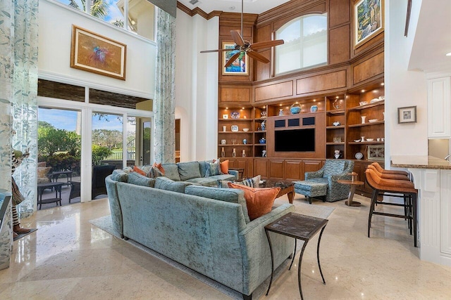 living room with crown molding, built in shelves, ceiling fan, and a high ceiling