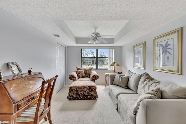 living area featuring visible vents, a textured ceiling, a raised ceiling, light colored carpet, and ceiling fan