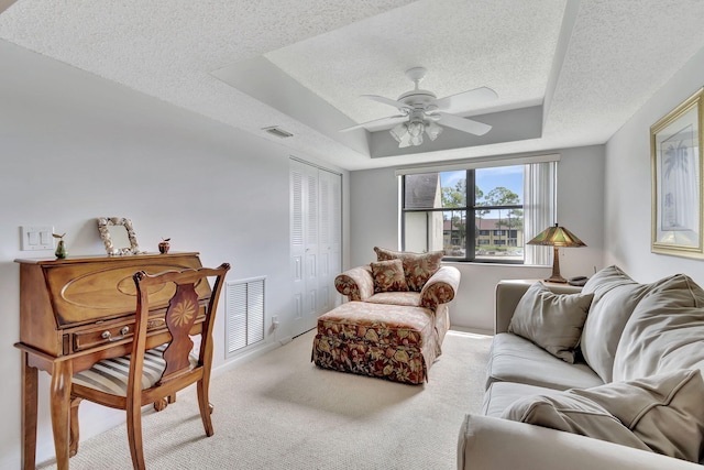 living room with ceiling fan, light carpet, a textured ceiling, and a tray ceiling