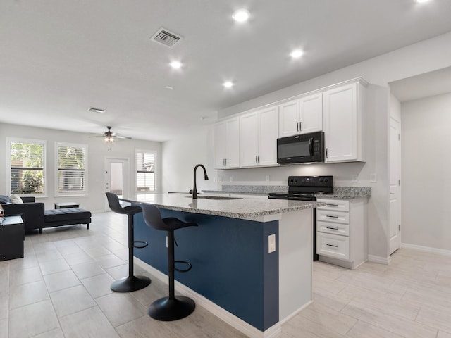 kitchen featuring light stone countertops, a kitchen island with sink, sink, black appliances, and white cabinets