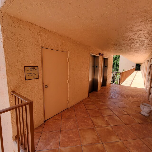 corridor with tile patterned flooring, a textured ceiling, and elevator