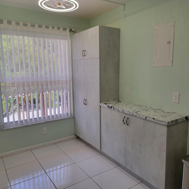 kitchen featuring electric panel, plenty of natural light, light stone counters, and light tile patterned floors