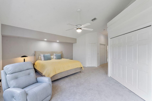 bedroom with vaulted ceiling, light carpet, ceiling fan, and multiple closets