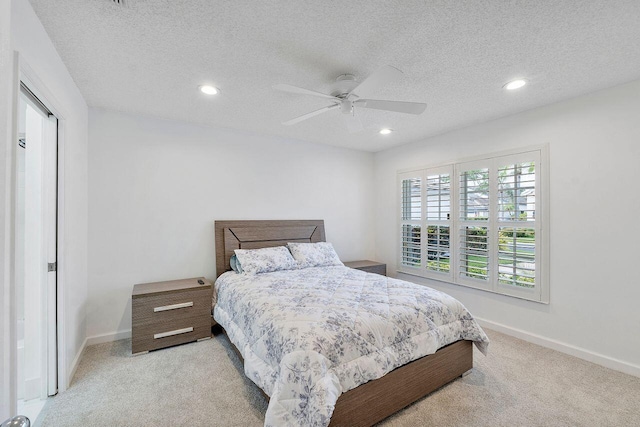 bedroom with ceiling fan, light colored carpet, and a textured ceiling