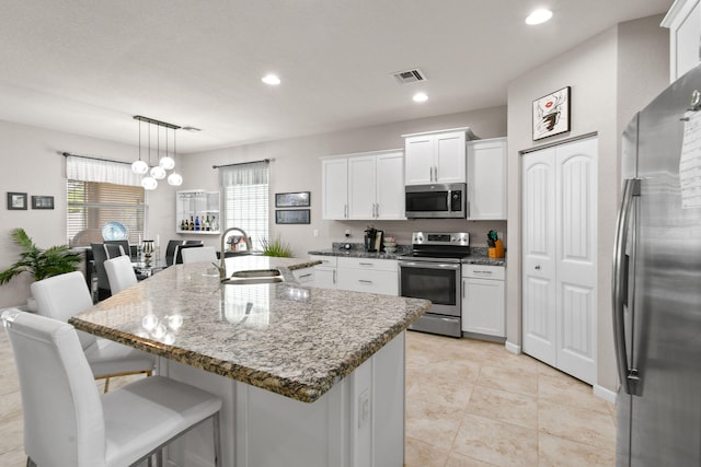 kitchen with white cabinets, stainless steel appliances, sink, an island with sink, and a breakfast bar