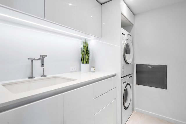 laundry area featuring cabinets, stacked washer / dryer, sink, and light tile patterned floors