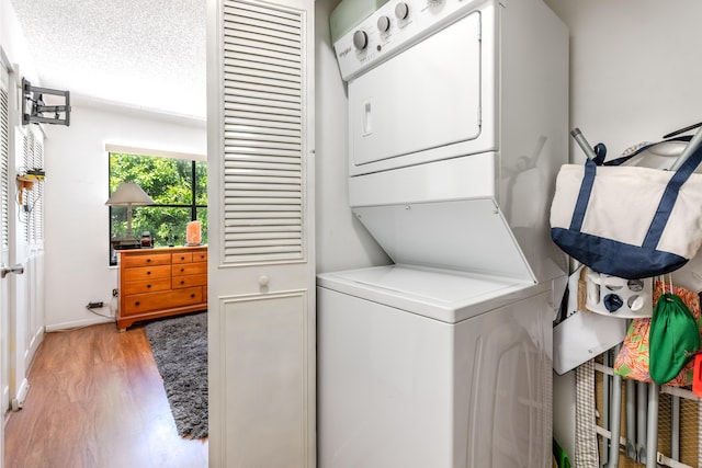 clothes washing area with hardwood / wood-style flooring, stacked washer and clothes dryer, and a textured ceiling