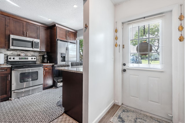 kitchen featuring backsplash, light stone countertops, stainless steel appliances, dark brown cabinetry, and a textured ceiling