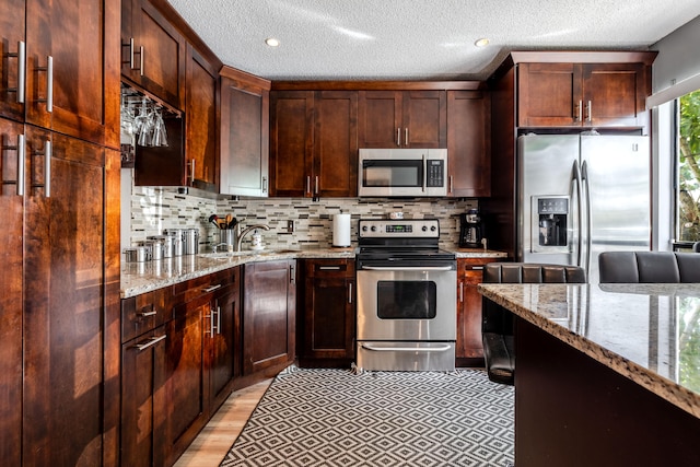 kitchen featuring light wood-type flooring, light stone counters, sink, decorative backsplash, and appliances with stainless steel finishes