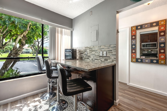 kitchen featuring light stone countertops, stainless steel appliances, wood-type flooring, tasteful backsplash, and a textured ceiling