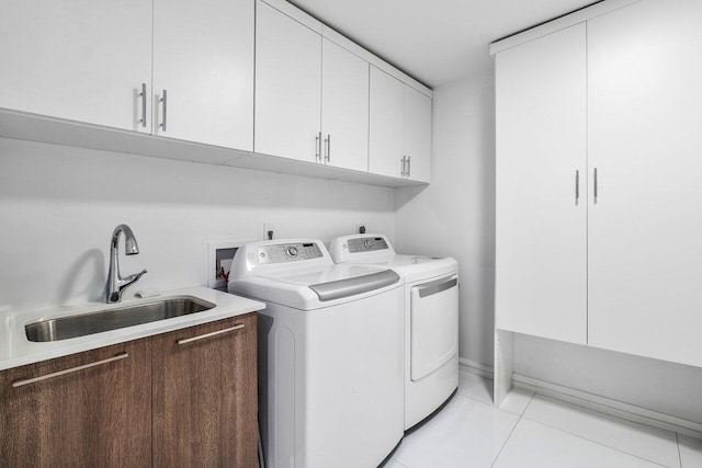 clothes washing area featuring light tile patterned floors, washing machine and dryer, cabinets, and sink