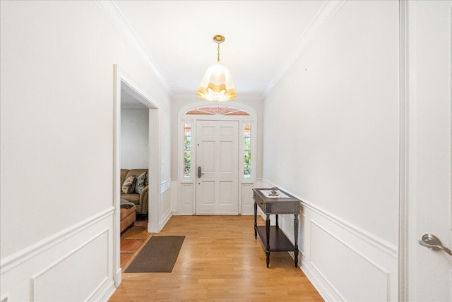 entryway featuring crown molding, a decorative wall, a wainscoted wall, and light wood finished floors