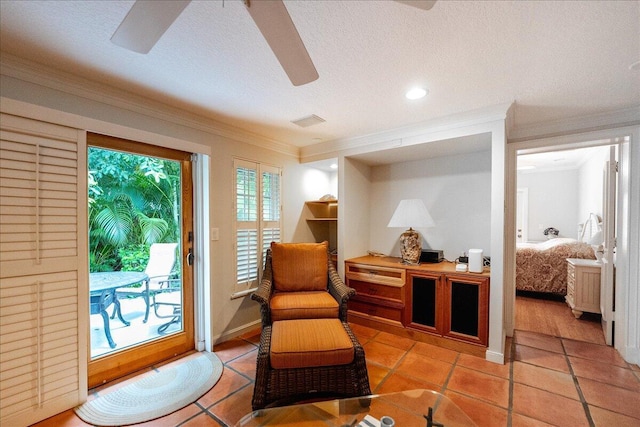 living area featuring light tile patterned floors, visible vents, ceiling fan, a textured ceiling, and crown molding