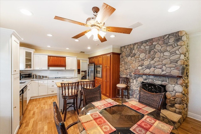 dining space featuring a ceiling fan, recessed lighting, ornamental molding, a stone fireplace, and light wood-type flooring