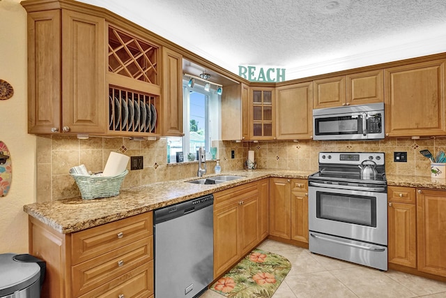 kitchen with a textured ceiling, light stone countertops, stainless steel appliances, sink, and light tile patterned flooring