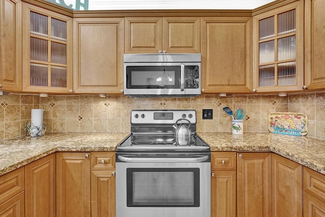 kitchen featuring stainless steel appliances, light stone countertops, and decorative backsplash